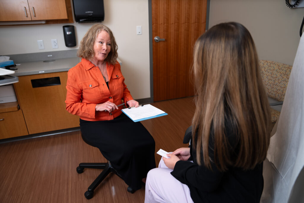 Photo for "Supporting Health by Screening for Social Needs" entry, featuring a patient in an exam room being asked questions by a healthcare provider.
